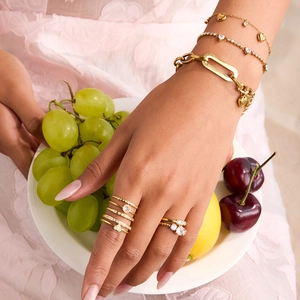 Detail of gold heart charm bracelets and zircon rings styled with fresh fruit bowl