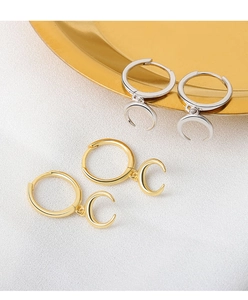 Detailed view of moon earrings in gold and silver finish on a luxury textured background