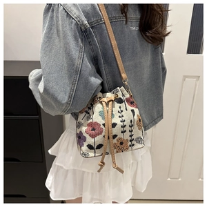 Close-up of woven drawstring bucket bag with colorful floral embroidery on a model
