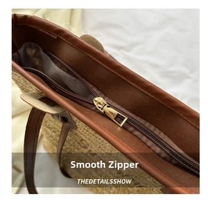 Detail of smooth metal zipper and brown leather trim on woven straw tote bag
