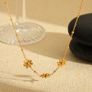 Golden stainless steel sunflower necklace with three daisies on a soft fabric background