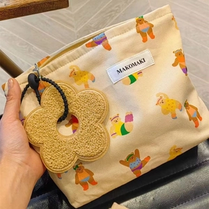 Detail showing beige canvas bag with cartoon bear pattern and plush flower zipper pull