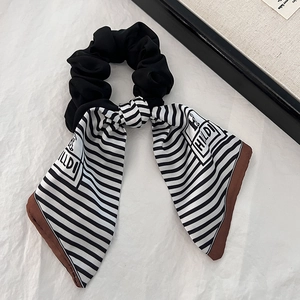 Detail of a black scrunchie with black and white striped ribbons and brown piping trim