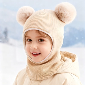 Close-up of a child wearing a beige fleece-lined knit balaclava hat with dual fur pom-poms