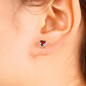 Close-up of heart-shaped red gemstone earrings in silver setting worn on ear lobe