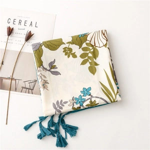 Detail of silk scarf with green leaves, blue flowers and navy tassel edges on table