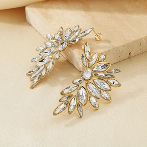 Macro detail of gold-plated leaf earrings with faceted clear crystals on stone base