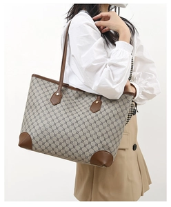 Brown monogram tote bag with leather handles shown on model wearing white shirt