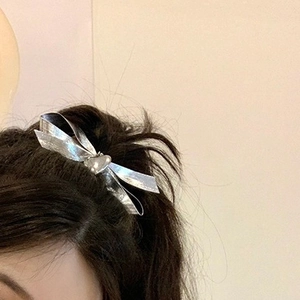 Silver heart bow hair clip with metallic luster worn by a model in a minimalist setting