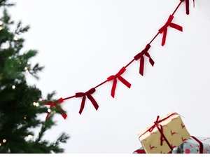 Detail of red velvet bow garland hanging against a festive white background with a Christmas tree