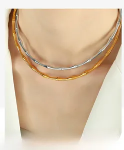 Detail of layered gold and silver bamboo-style necklaces on a model in a white blazer