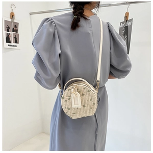 Detail of woven straw circle bag with floral embroidery and white leather strap