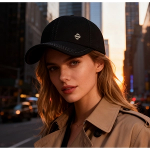 Close-up of black cotton baseball cap with a circular metal logo during sunset