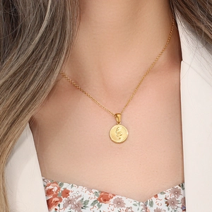 Detailed view of a gold circular pendant necklace featuring an engraved snake motif