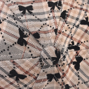Close-up of classic plaid fabric texture with small black bow pattern on newsboy cap