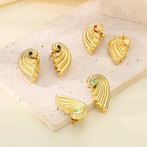 Three pairs of gold wing earrings with red, green, and black stones on stone background