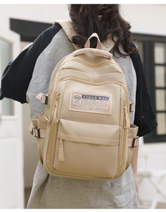 Close-up of beige nylon backpack worn by model, showing branding patch and soft texture