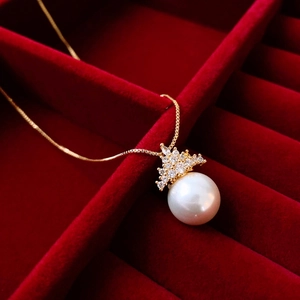 Detailed view of crown-shaped zircon and white pearl necklace in a red velvet jewelry box