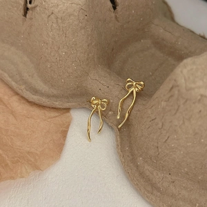 Macro shot of elegant golden ribbon bow dangle earrings on rustic textured background