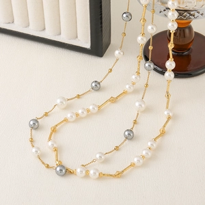 Detailed view of layered white and grey pearls with gold metal accents on white leather