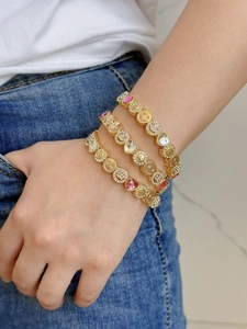 Close-up of three-piece stacked gold charm bracelets with pink enamel smiley faces and hearts