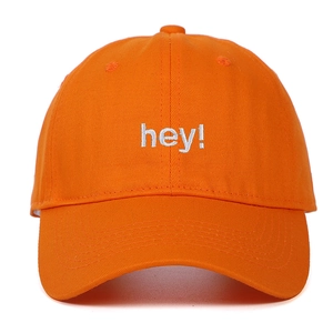 Détail d'une casquette en coton orange avec broderie blanche 'hey!' sur le devant