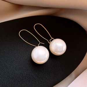 Macro detail of gold geometric pearl earrings on black stand with silk background