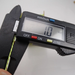 Macro view of digital caliper measuring 1mm diameter light green golden metallic thread