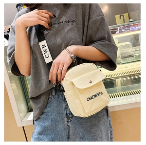 Close-up of beige canvas crossbody bag with adjustable wide black strap and text detail