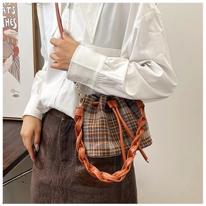 Detail of plaid wool bucket bag featuring woven leather strap and drawstring closure