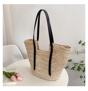 Détail d'un grand sac cabas en paille tissé à la main avec anses noires sur table blanche