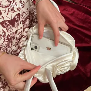 Internal view of rose-shaped white satin handbag showing capacity with a mobile phone