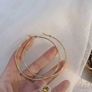 Detailed close-up of large polished gold hoop earrings held against soft white fabric background