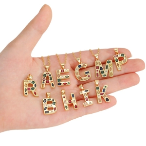 Golden alphabet pendants with colorful zircon stones on thin gold chains held by hand