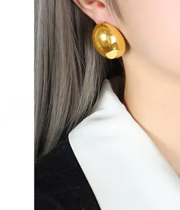 Close-up of model wearing large oval gold stainless steel earrings with mirror finish