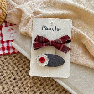 Detail of red plaid bow hairpin and grey oval fabric clip with a crochet flower