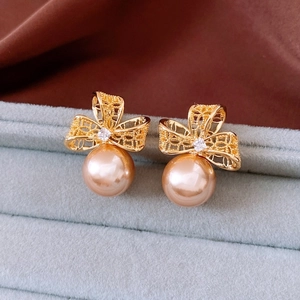 Macro view of gold bow knot pearl earrings displayed on a grey velvet jewelry box