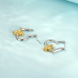 Two-tone stainless steel heart earrings with gold bee charms on blue background