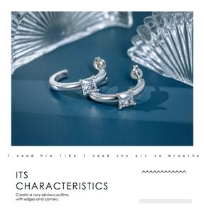Detail of silver C-shaped earrings with square zircon stones on a blue background