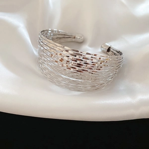 Close-up of a silver multi-layer ripple texture open bangle on white silk fabric