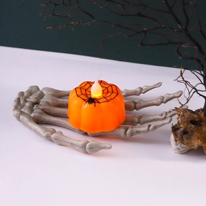 Dettaglio della candela LED a zucca arancione con ragnatela sorretta da una mano di scheletro