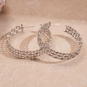 Detailed close-up of silver braided hoop earrings on a textured neutral surface