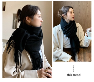 Detail view of a soft black cashmere-like scarf with fringe on a female model