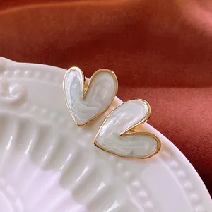 Elegant gold heart earrings with white marble texture inlay on a decorative ceramic plate