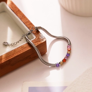 Detail of silver snake chain bracelet with multi-colored zircon stones on a wood tray