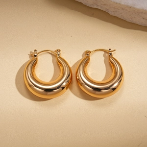 Minimalist thick gold round earrings with metallic shine on a beige stone surface