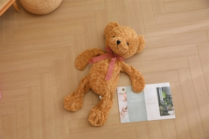 Close-up of brown curly plush teddy bear with a red checkered bow on wooden floor