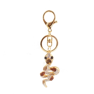 Cute golden zodiac snake keychain with white and orange rhinestones on white background