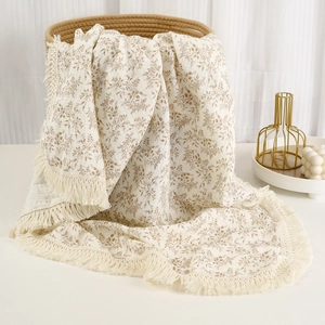Detail of floral muslin baby blanket with fringe trim and soft cotton texture