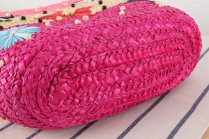 Détail macro d'un sac bohème en paille tressée rose fuchsia et beige avec perles